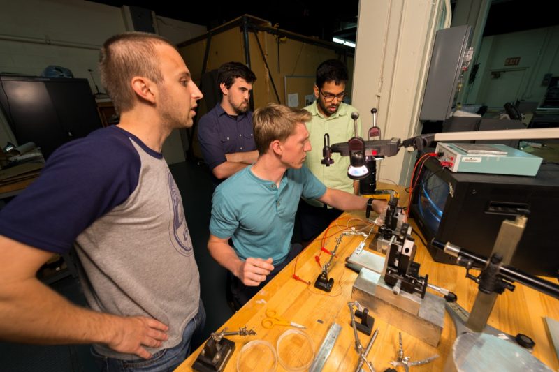 Undergraduate research students Lee Organski (center left) and Jon Schwaner (center right) gather round an instrumentation repair station.