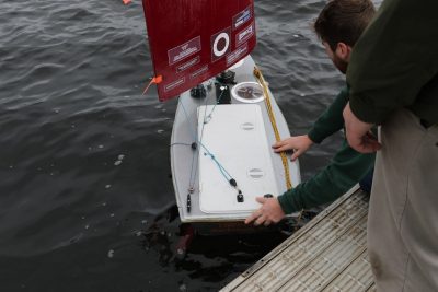 Student places the SailBot boat, Theseus into the water.