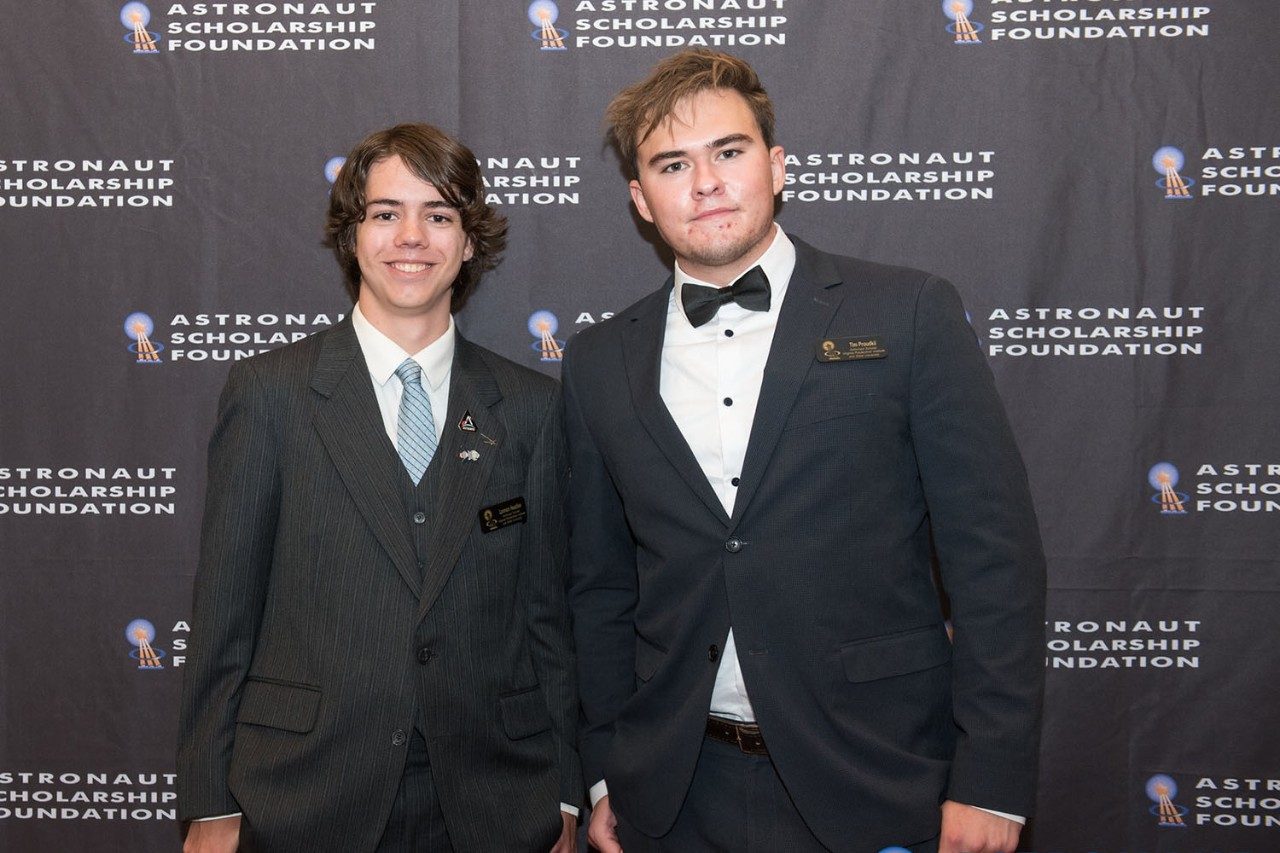Two students, each wearing suits, pose in front of a banner for the Astronaut Scholarship Foundation.