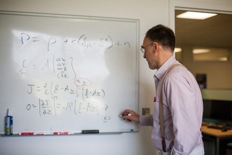 In the photo, Mark Psiaki writes several formulas on a whiteboard in his office.